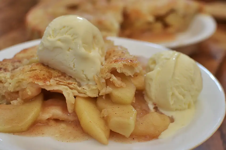 Warm apple pie served with two scoops of vanilla ice cream.