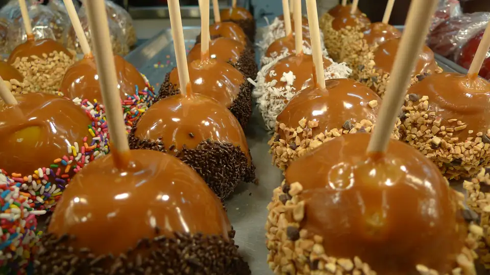 Rows of glossy caramel apples rolled in sprinkles, coconut and chopped nuts.
