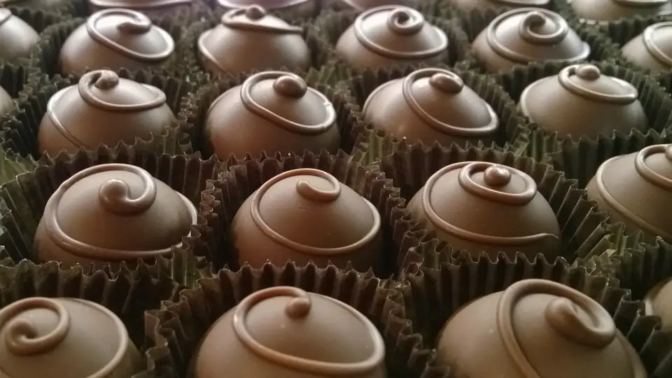 Rows of hand-finished chocolates with piped swirls, each in a paper cup.