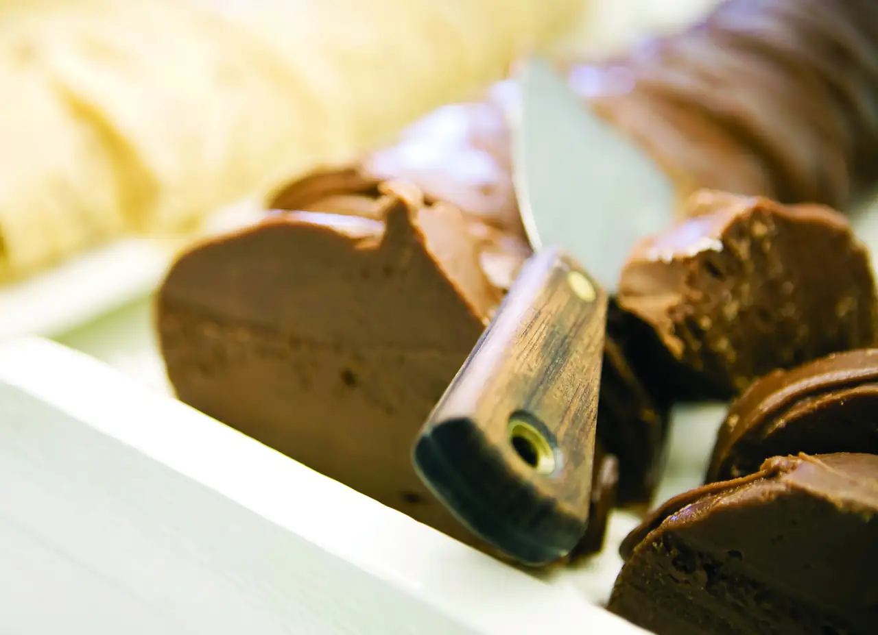 A loaf of chocolate fudge being sliced on a marble slab.