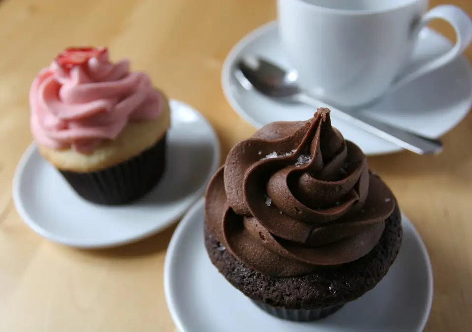 A chocolate cupcake and a strawberry cupcake set out with a cup of coffee.