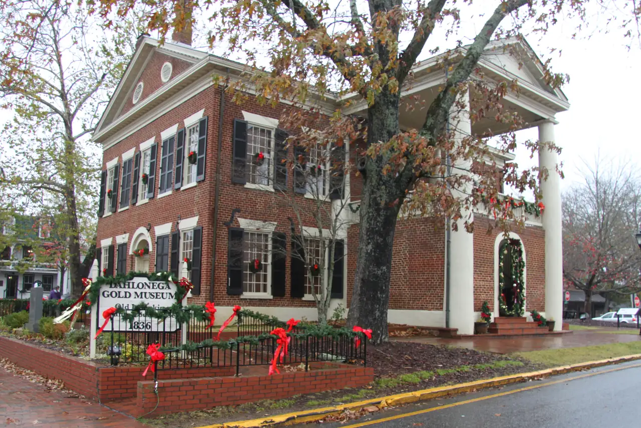 The red-brick Gold Museum on Dahlonega's square wrapped in evergreen garland and red bows on a rainy late-autumn day.