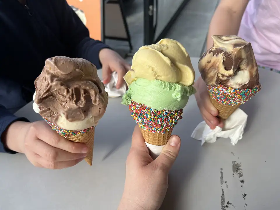 Three scoops-on-cones with rainbow-sprinkle rims, held up over a cafe table.