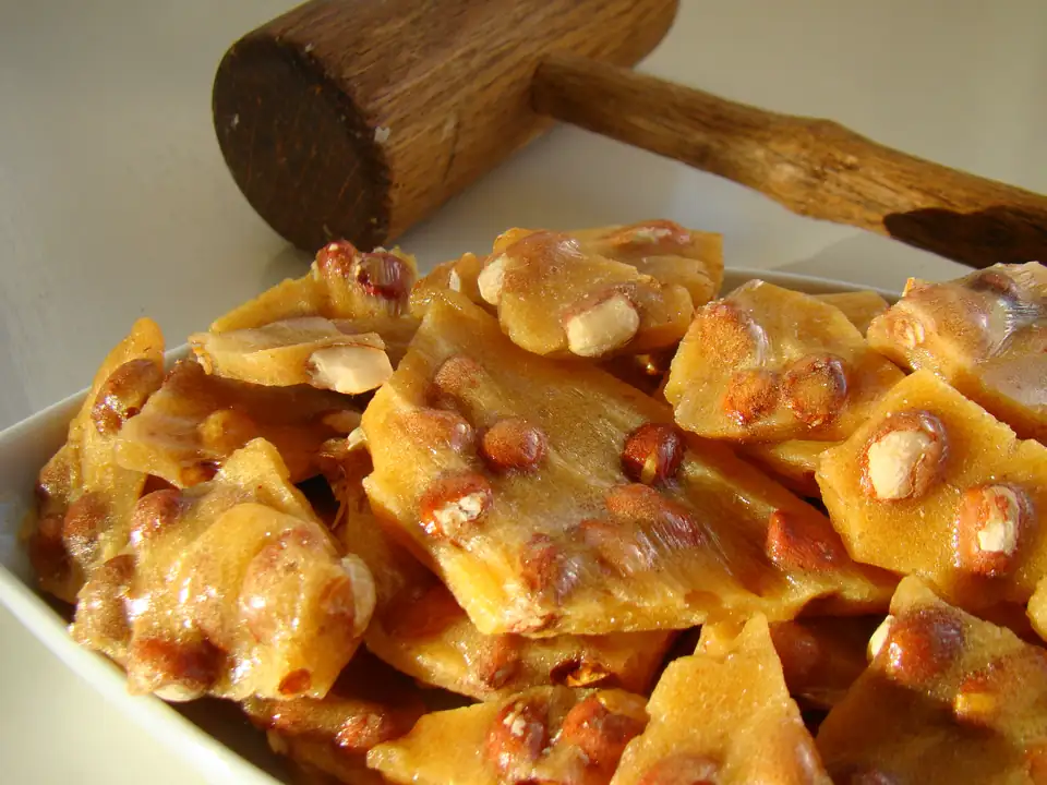Golden peanut brittle broken into shards, with a wooden mallet.