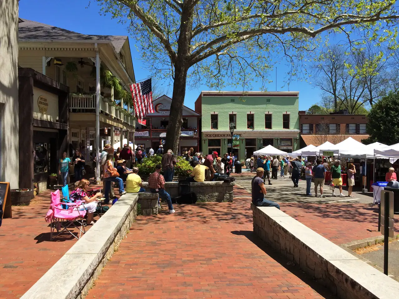 A crowded spring afternoon on Dahlonega's Public Square, with the mint-green Ice Cream Parlor building behind white market tents and people strolling the brick plaza.