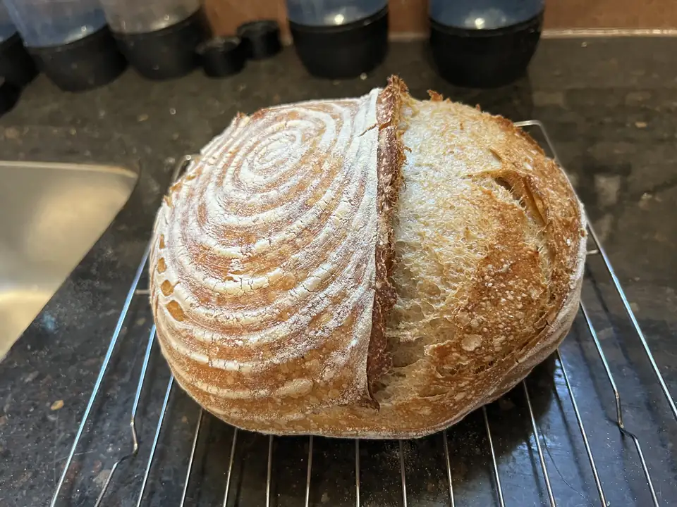 A crusty sourdough loaf with a floured spiral pattern, cooling on a rack.