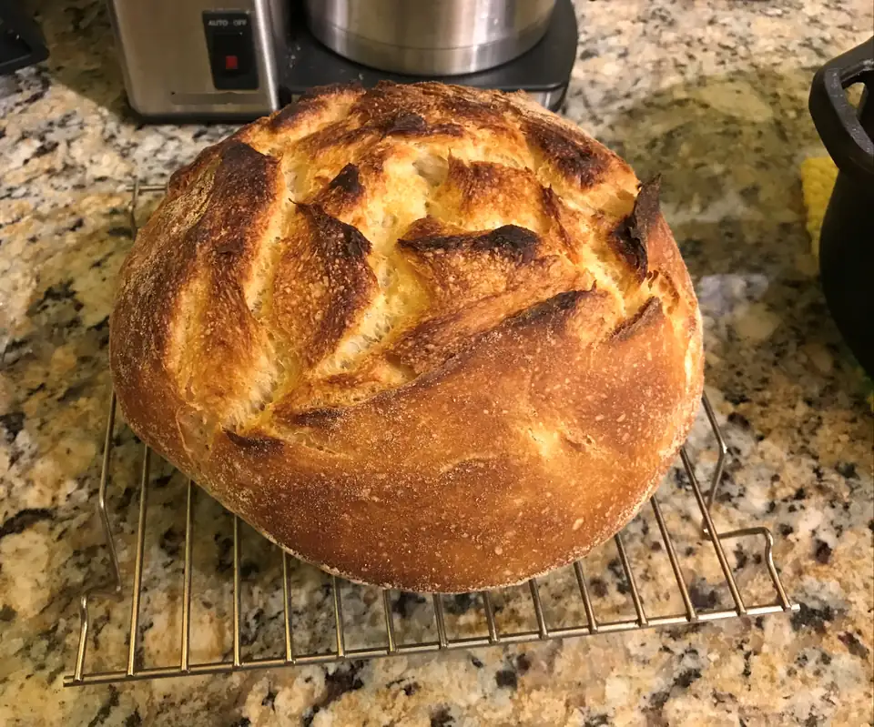 A dark-crusted round loaf of bread cooling on a wire rack.